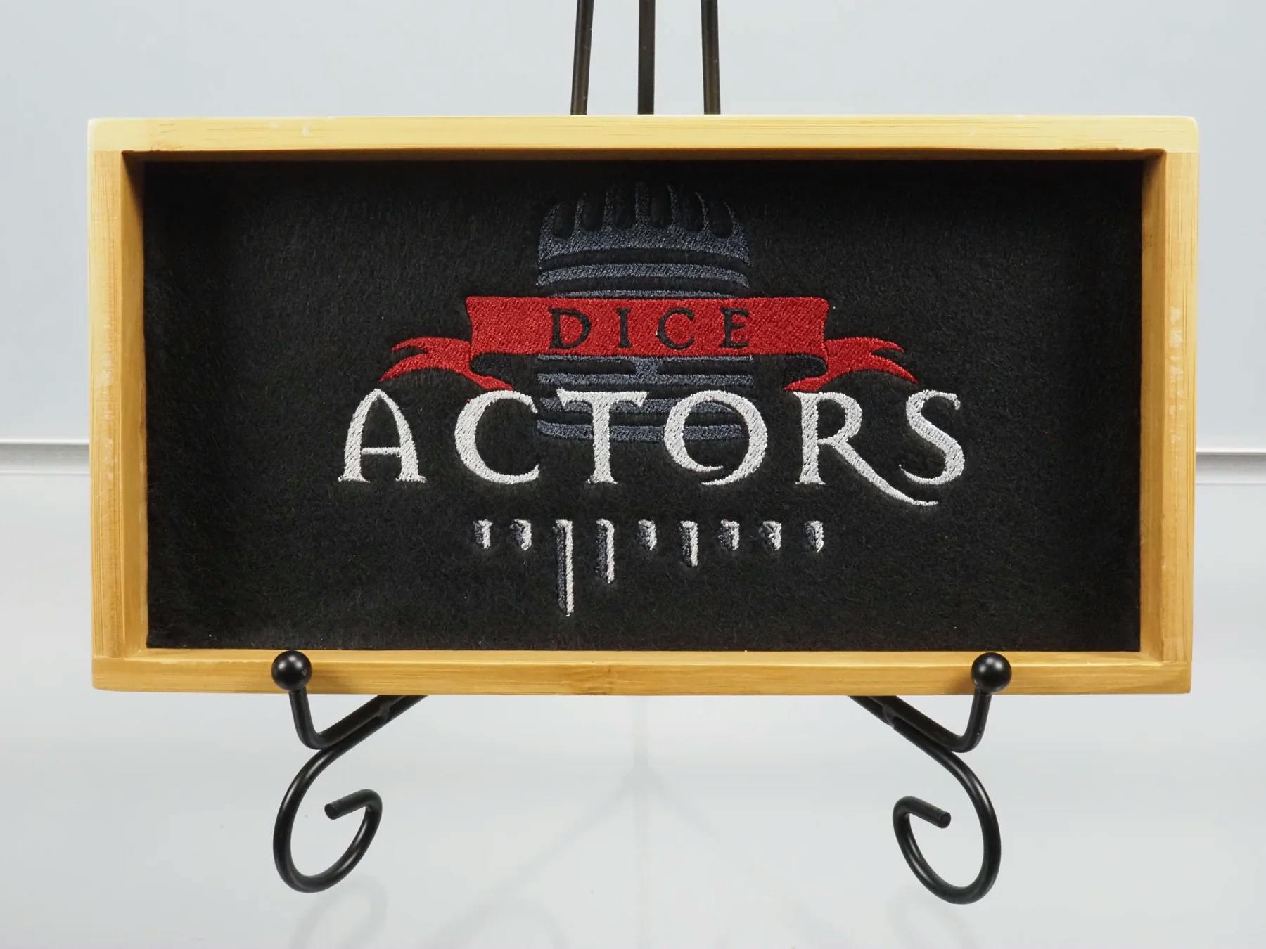 Ein silbriger Schriftzug, gekrönt von einem roten Banner. Im Hintergrund sind schemenhaft die Umrisse eines Mikrofons zu erkennen. Unser Dice-Actors-Logo im Dice Tray.