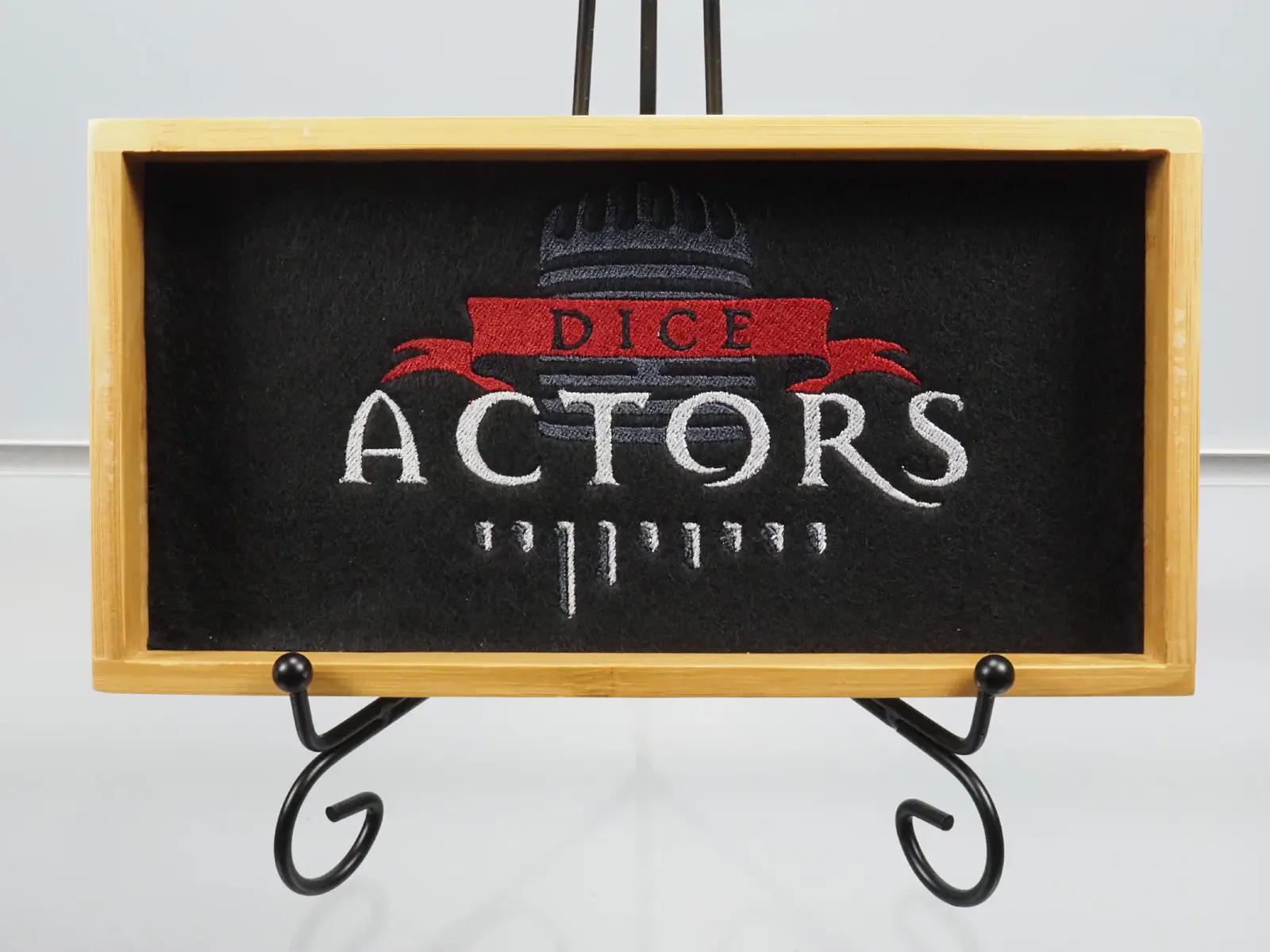 Ein silbriger Schriftzug, gekrönt von einem roten Banner. Im Hintergrund sind schemenhaft die Umrisse eines Mikrofons zu erkennen. Unser Dice-Actors-Logo im Dice Tray.