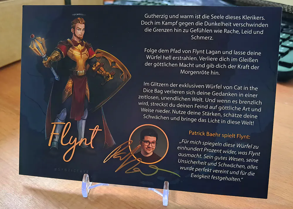 Eine Karte auf der Flynt abgebildet ist. Daneben ein Text über die Würfel und Patzes Gedanken zu den Würfeln. Außerdem ein kleines Foto von Patze und eine goldene Unterschrift.