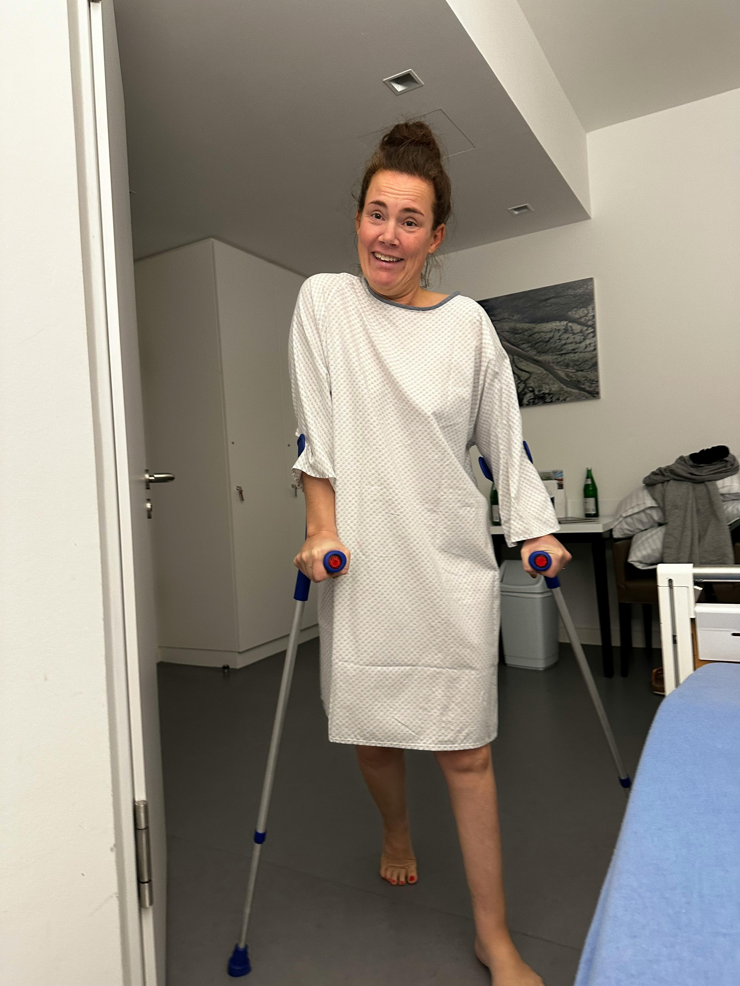Ich stehe mit Krücken und OP Hemd in einem Krankenhauszimmer.