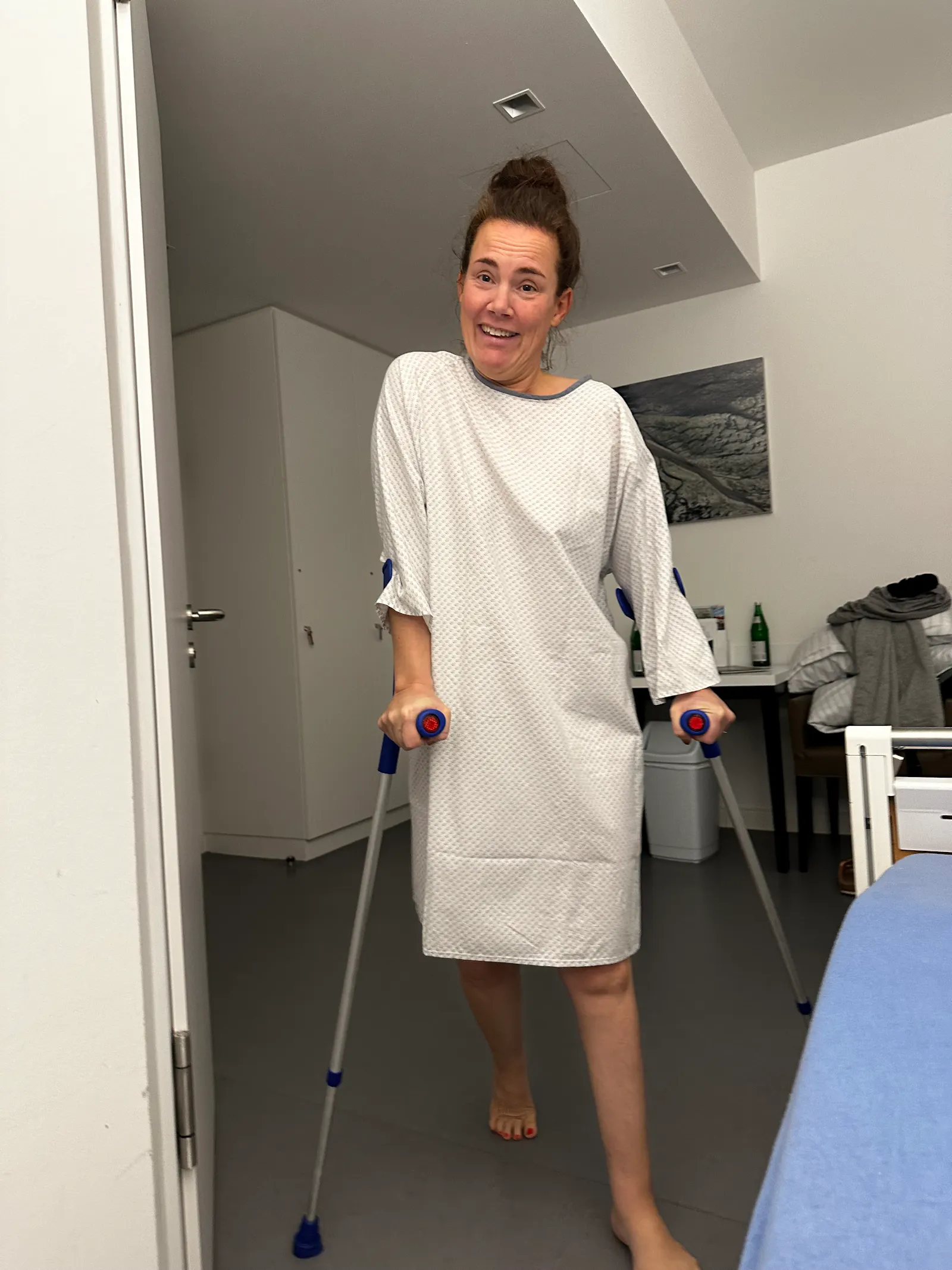 Ich stehe mit Krücken und OP Hemd in einem Krankenhauszimmer.