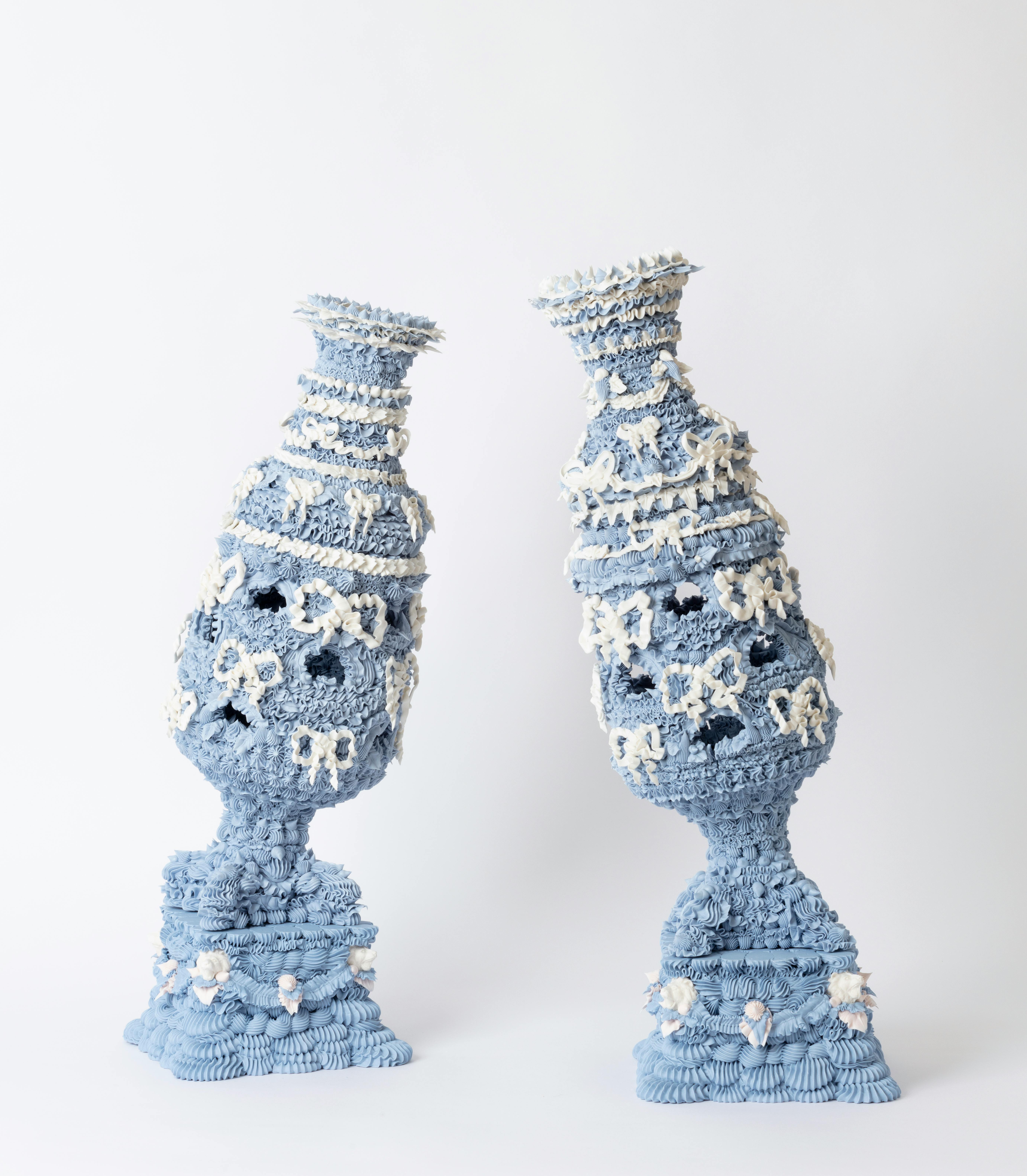 2 ceramic vases leaning towards each other. Each vase is light blue with piped details and white bow decorations.