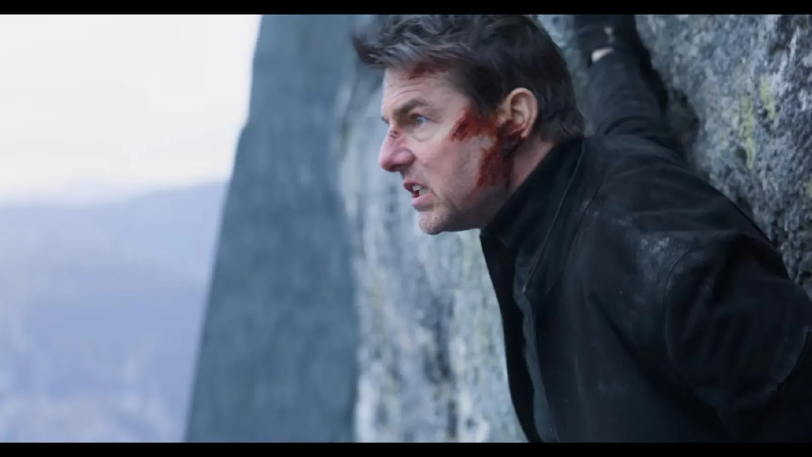 Screenshot aus dem Film "Mission Imossible - Fallout": Tom Cruise  mit blutverschmiertem Gesicht halbnah in einer Felswand, er starrt nach links mit einer Grimasse wie ein Gorilla wütender Gorilla, da ist aber nichts.