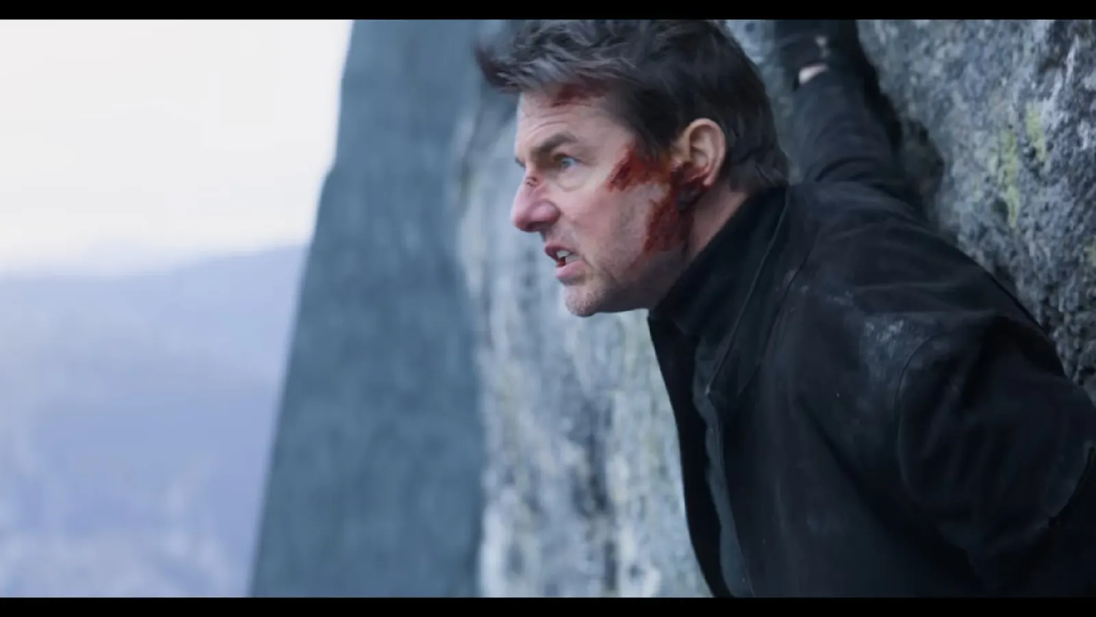 Screenshot aus dem Film "Mission Imossible - Fallout": Tom Cruise mit blutverschmiertem Gesicht halbnah in einer Felswand, er starrt nach links mit einer Grimasse wie ein Gorilla wütender Gorilla, da ist aber nichts.