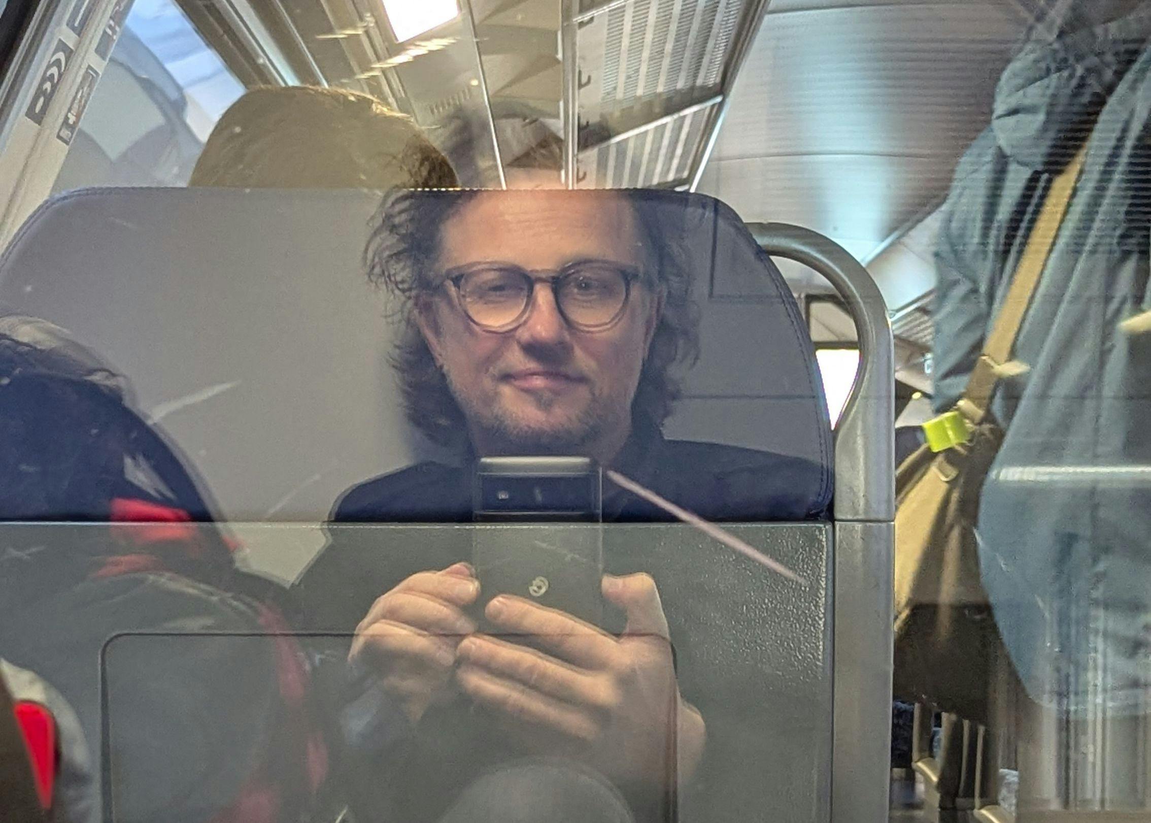 Ein Selfie von mir. Ich sitze in einem Zug und spiegle mich in der Scheibe. Dahinter befindet sich die 1. Klasse.