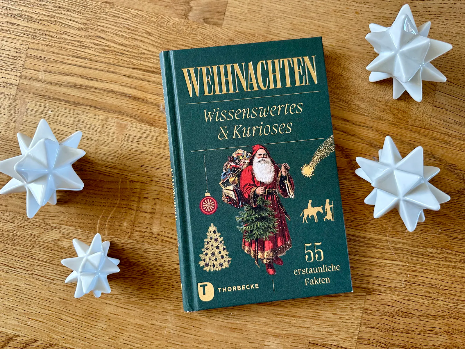 Buch "Weihnachten - Wissenswertes & Kurioses" auf einem Holztisch neben weißen Porzellan-Sternen.