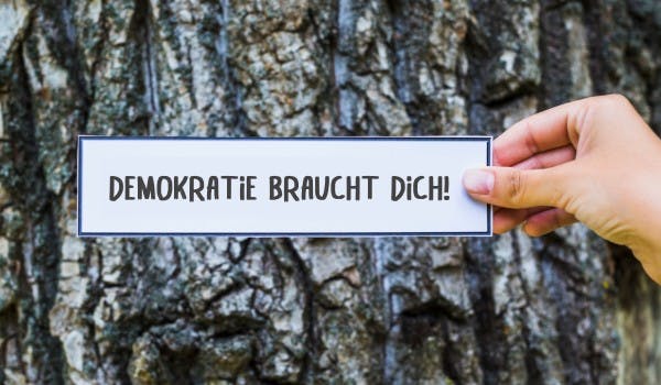 [Ein Schild vor einem Baum, auf dem steht "Demokratie braucht dich!"]