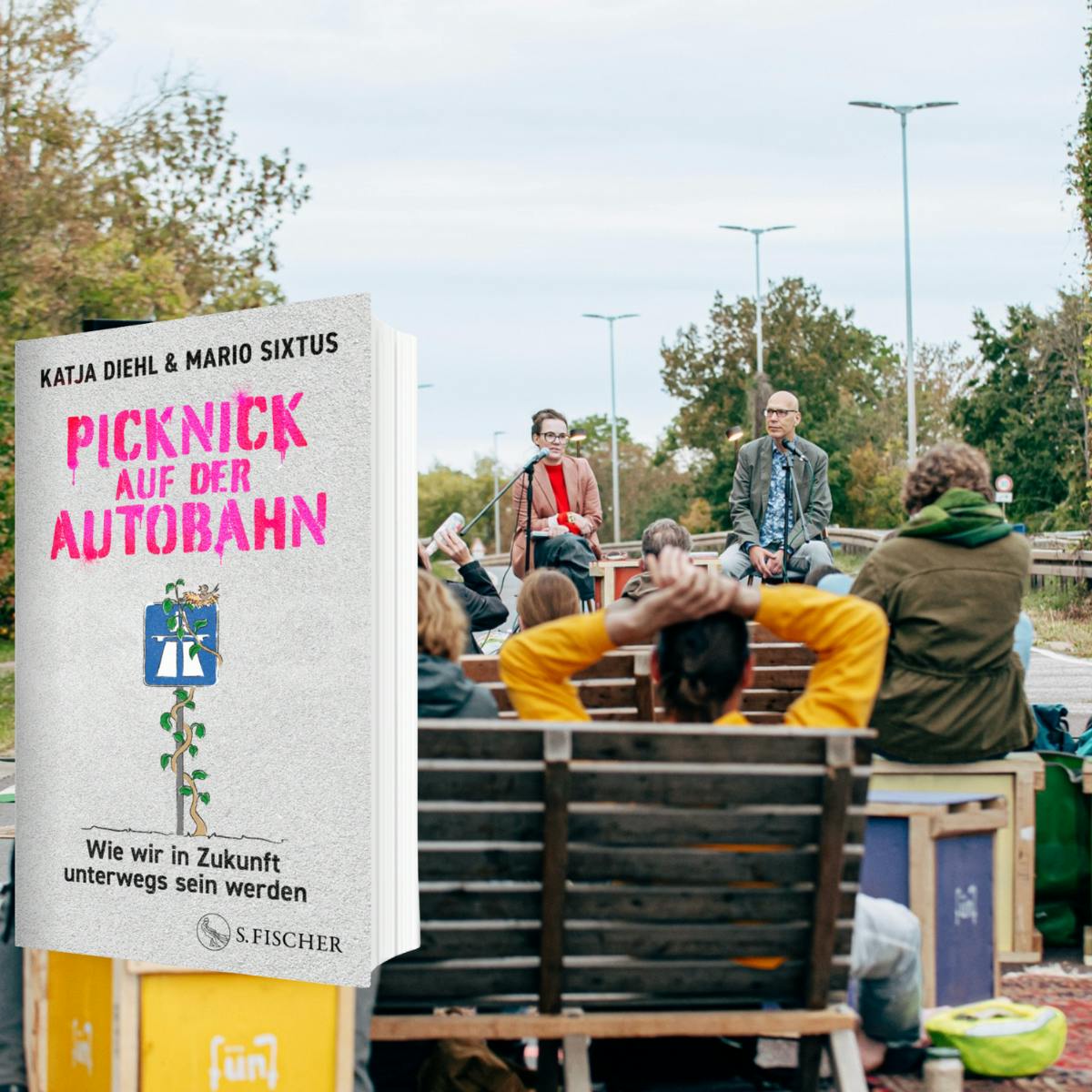 Ein Schnappschuss von der Lesung auf der Autobahn mit vielen Menschen im Vordergrund, die auf Hockern und Bänken sitzen, Mario und mir auf der Bühne und dem Buch.