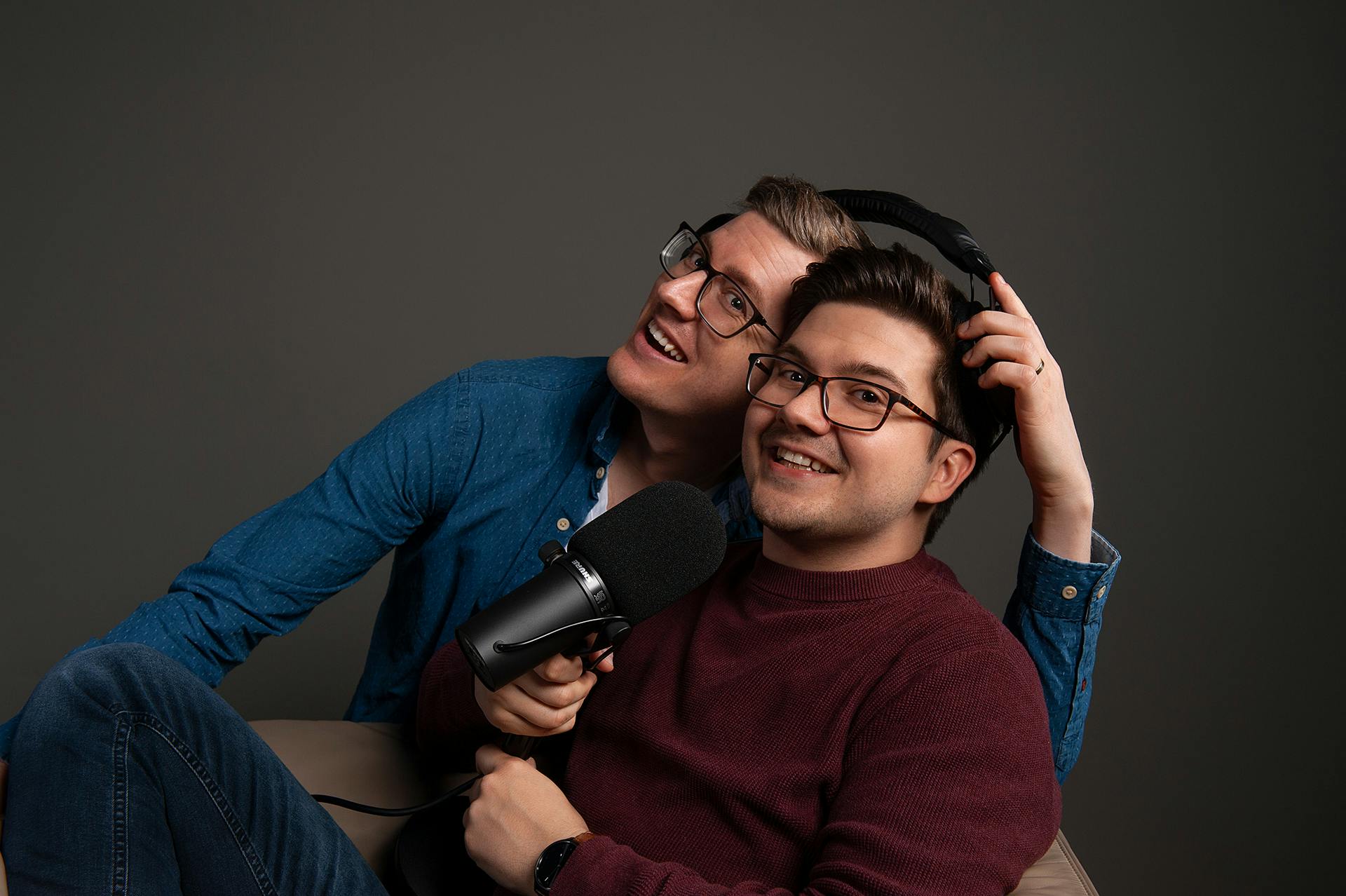 Tim und Patze, die sich einen Bügelkopfhörer teilen und ein Mikrofon in der Hand halten.