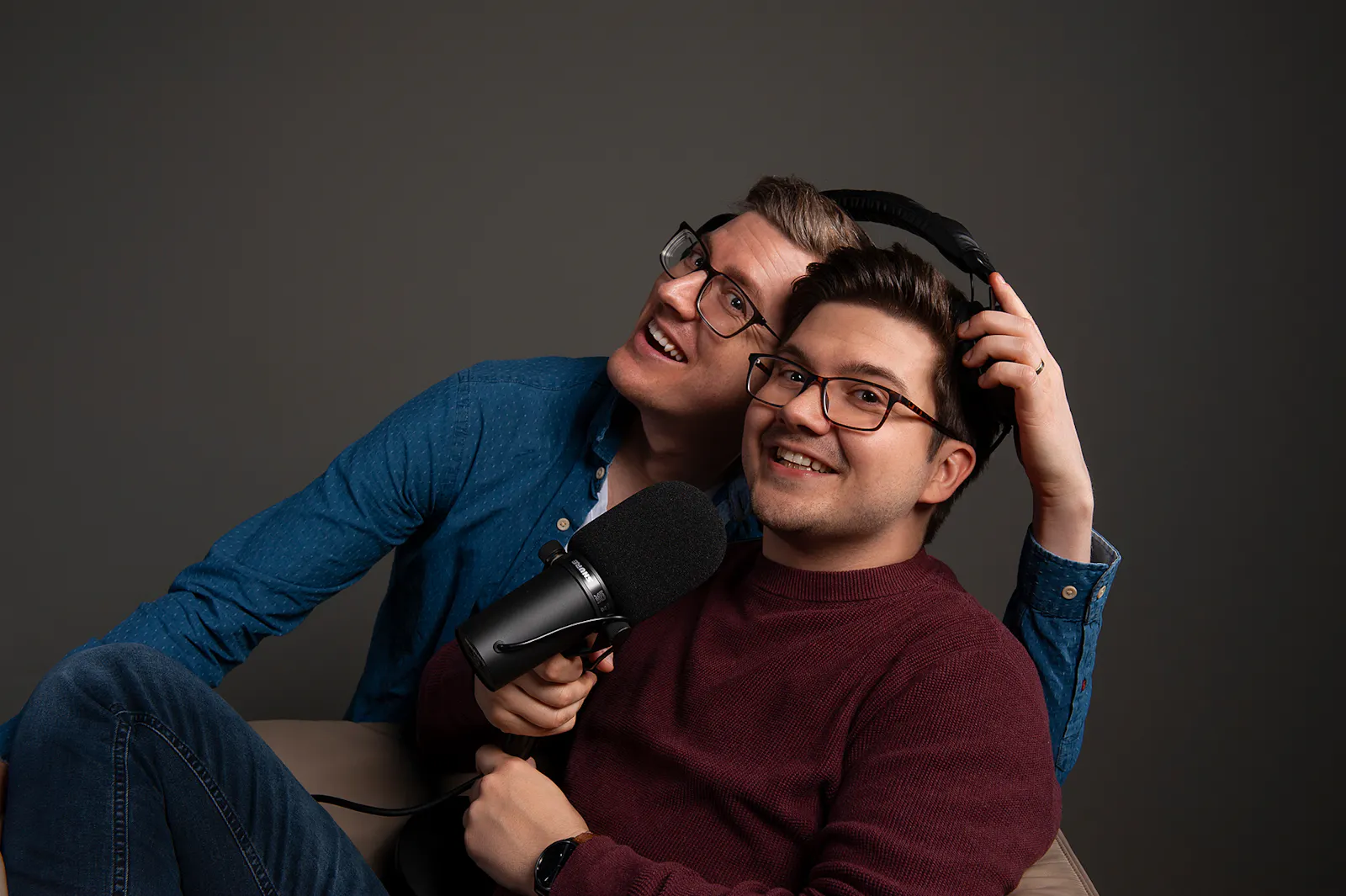 Tim und Patze, die sich einen Bügelkopfhörer teilen und ein Mikrofon in der Hand halten.