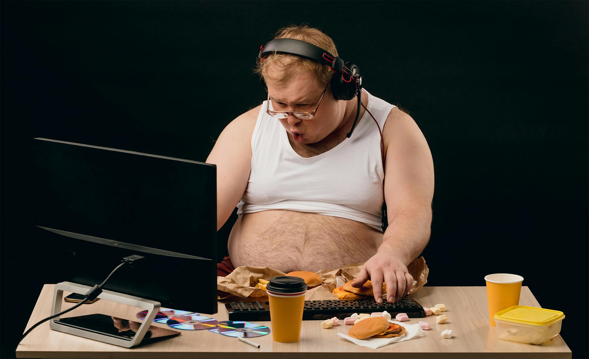 Ungeplegter, übergewichtiger Mann vor seinem Computer mit Kopfhörer und Mikofon.