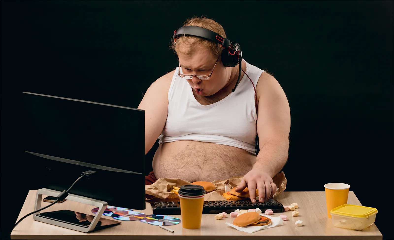 Ungeplegter, übergewichtiger Mann vor seinem Computer mit Kopfhörer und Mikofon.