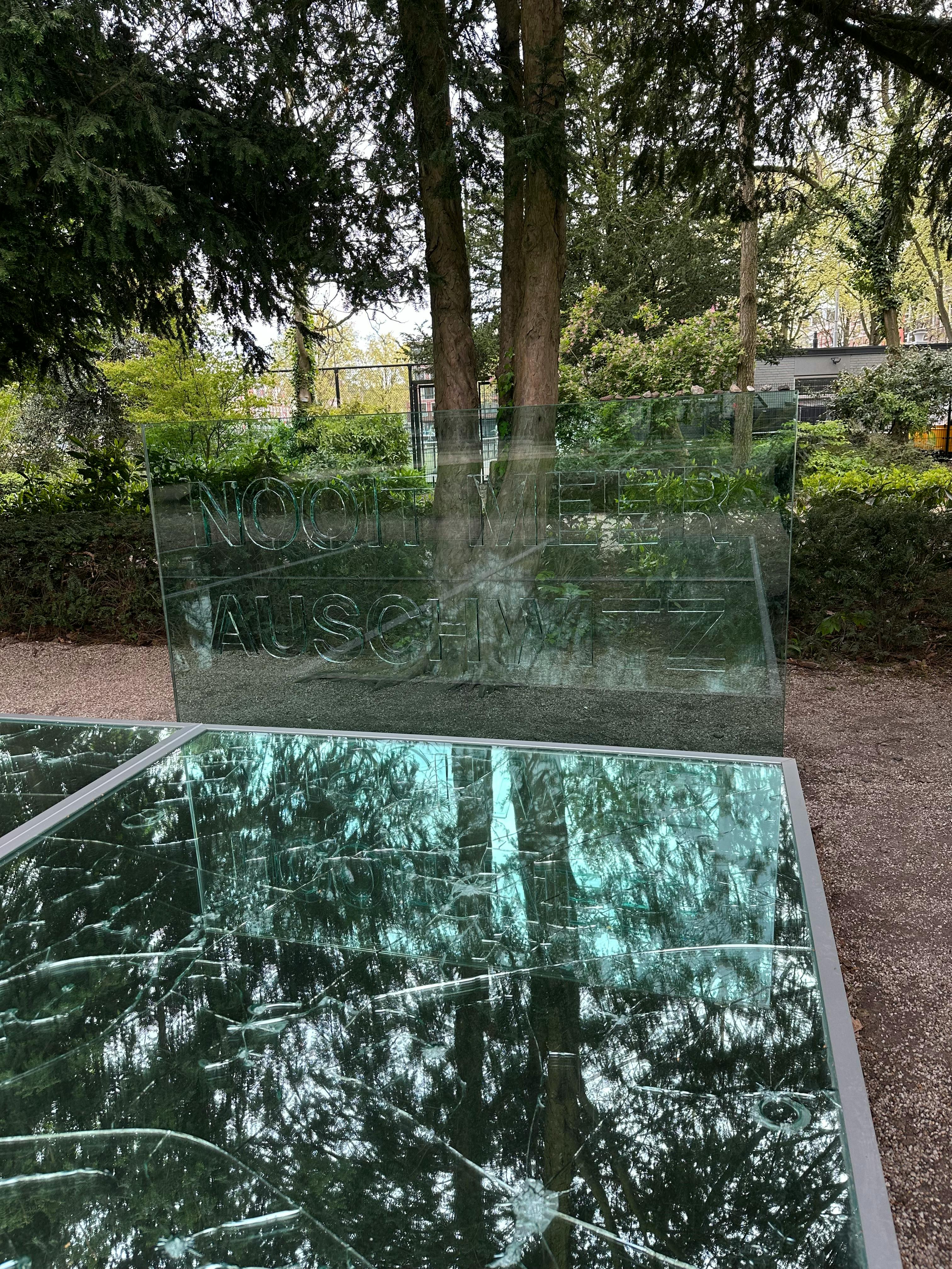 Das Auschwitz-Denkmal im Wertheim-Park, einem der ältesten Parks in Amsterdam. Eine vom Boden leicht erhöhte Fläche aus Spiegeln. In den Spiegeln sind Risse und Einschläge zu sehen, so dass der Himmel und die Umgebung sich darin gebrochen widerspiegeln. Am Kopfende rechts ist eine Glasscheibe auf der "Nooit meer Auschwitz" steht - Nie wieder Auschwitz.