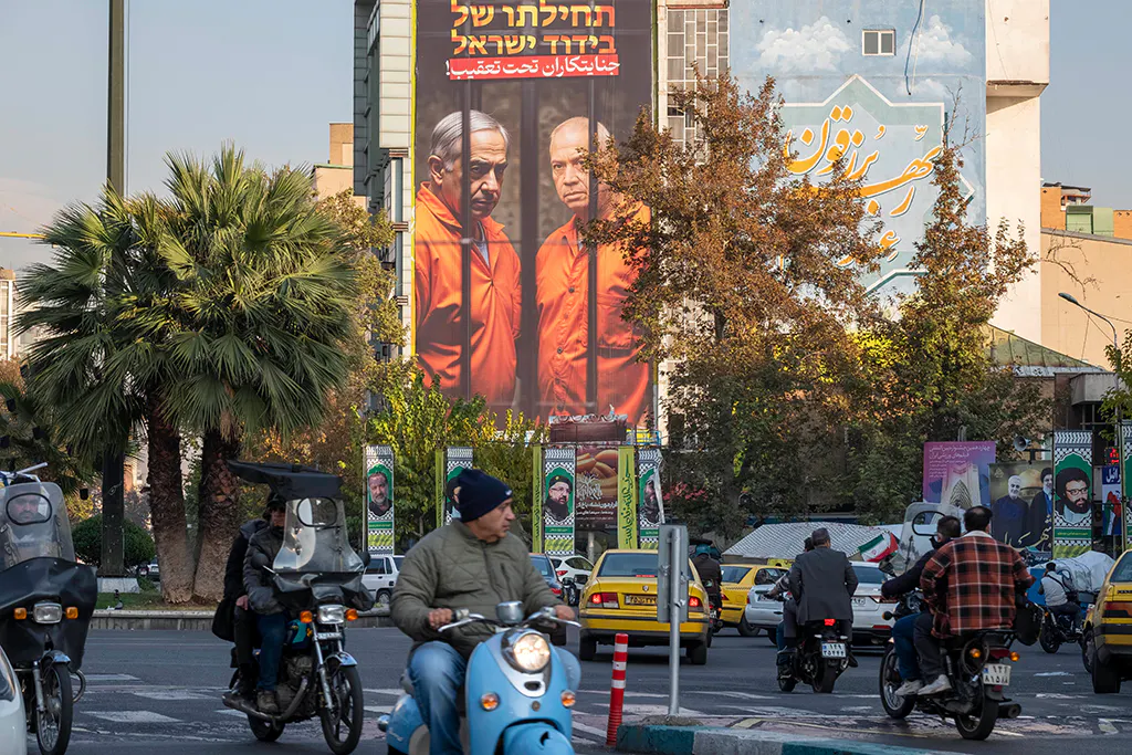 Straßenszene in Teheran mit einem sehr großen Plakat mit Netanyahu und Gallant in Sträflingskleidung hinter Gittern.