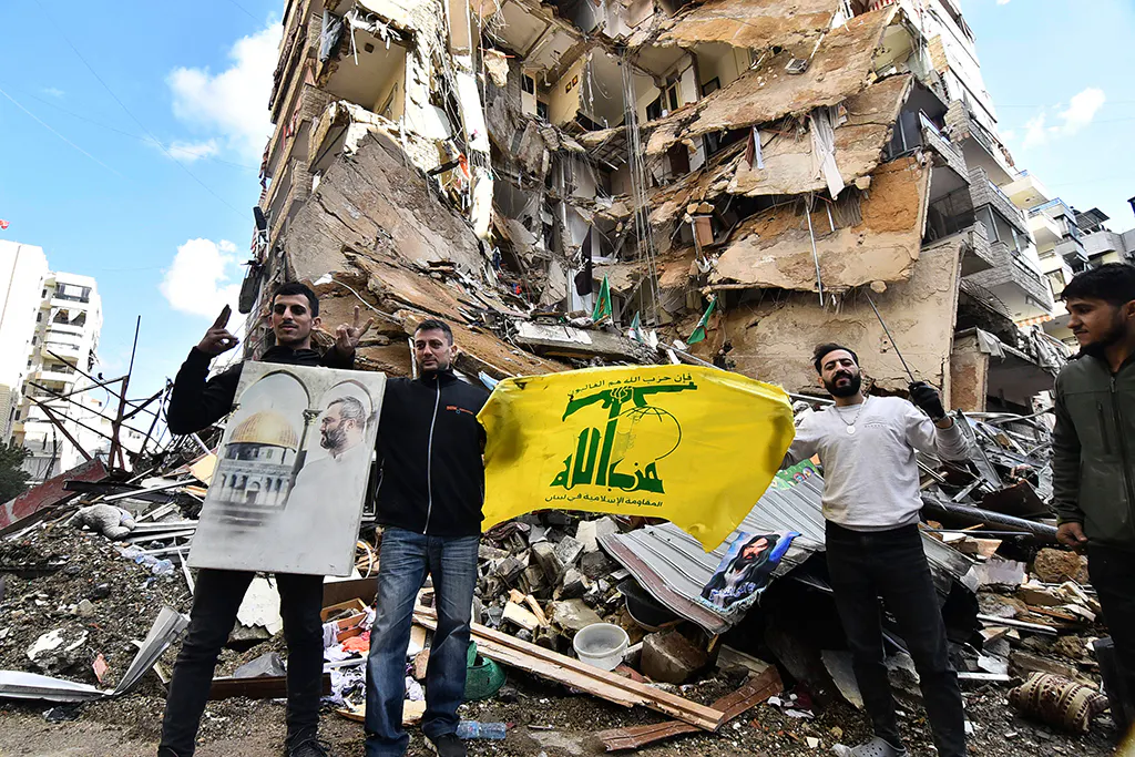 Männer posieren mit der Flagge der Hisbollah vor einem zerstörten Hochhaus in Beirut.