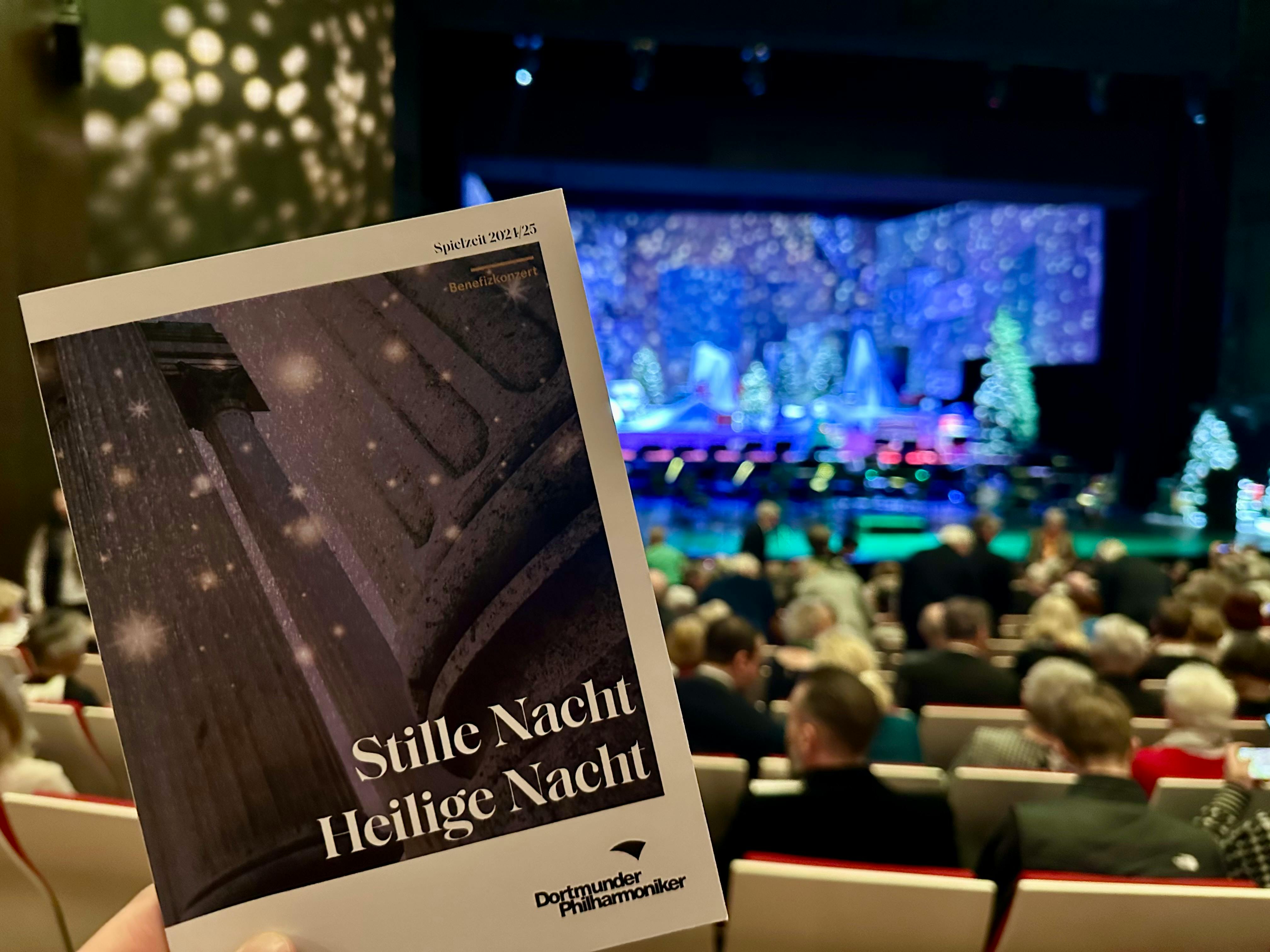 Programmheft vom Konzert "Stille Nacht, Heilige Nacht" der Dortmunder Philharmoniker. Im Hintergrund sieht man das Publikum und die Bühne vor Vorstellungsbeginn.