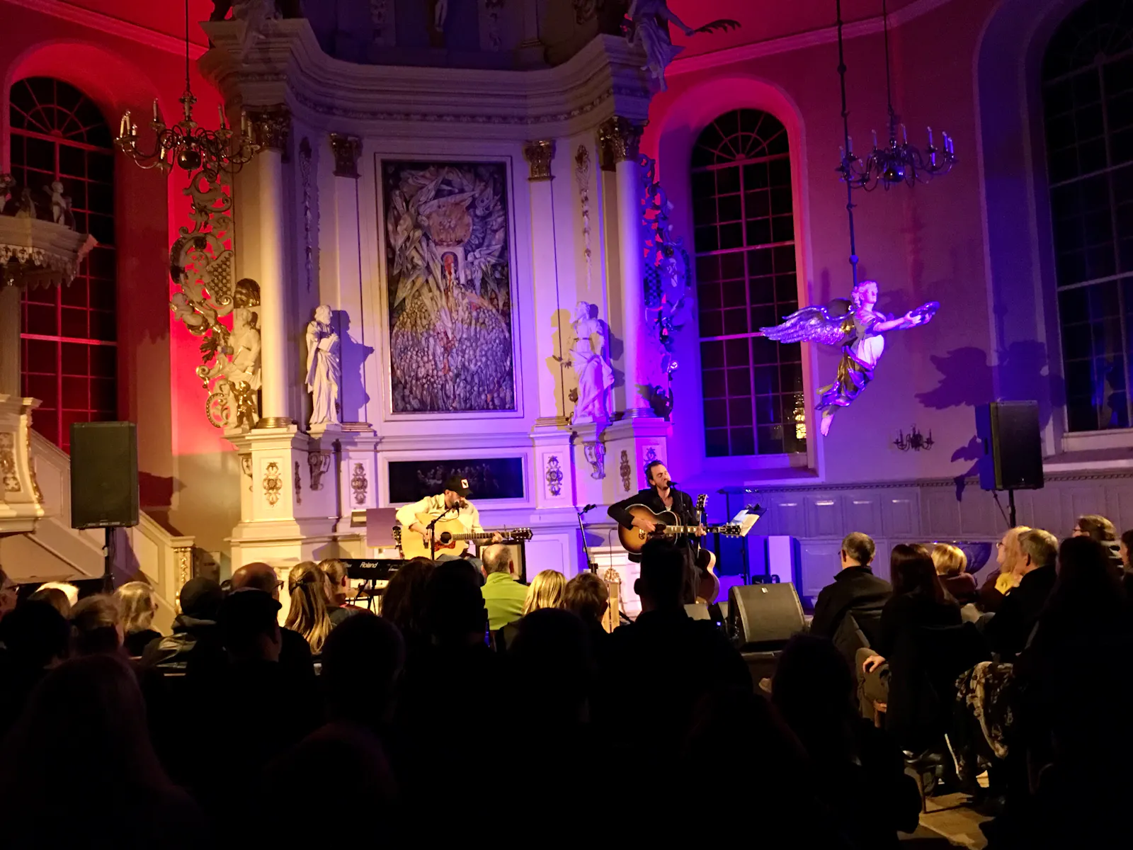 Publikum und zwei Musiker in einer festlich ausgeleuchteten Kirche.