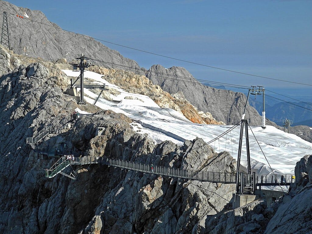 Auf diesen Foto sieht man die Hängebrücke am Dachstein. Im Hintergrund liegen schneebedeckte Flächen des Gletschers und felsige Berggipfel.