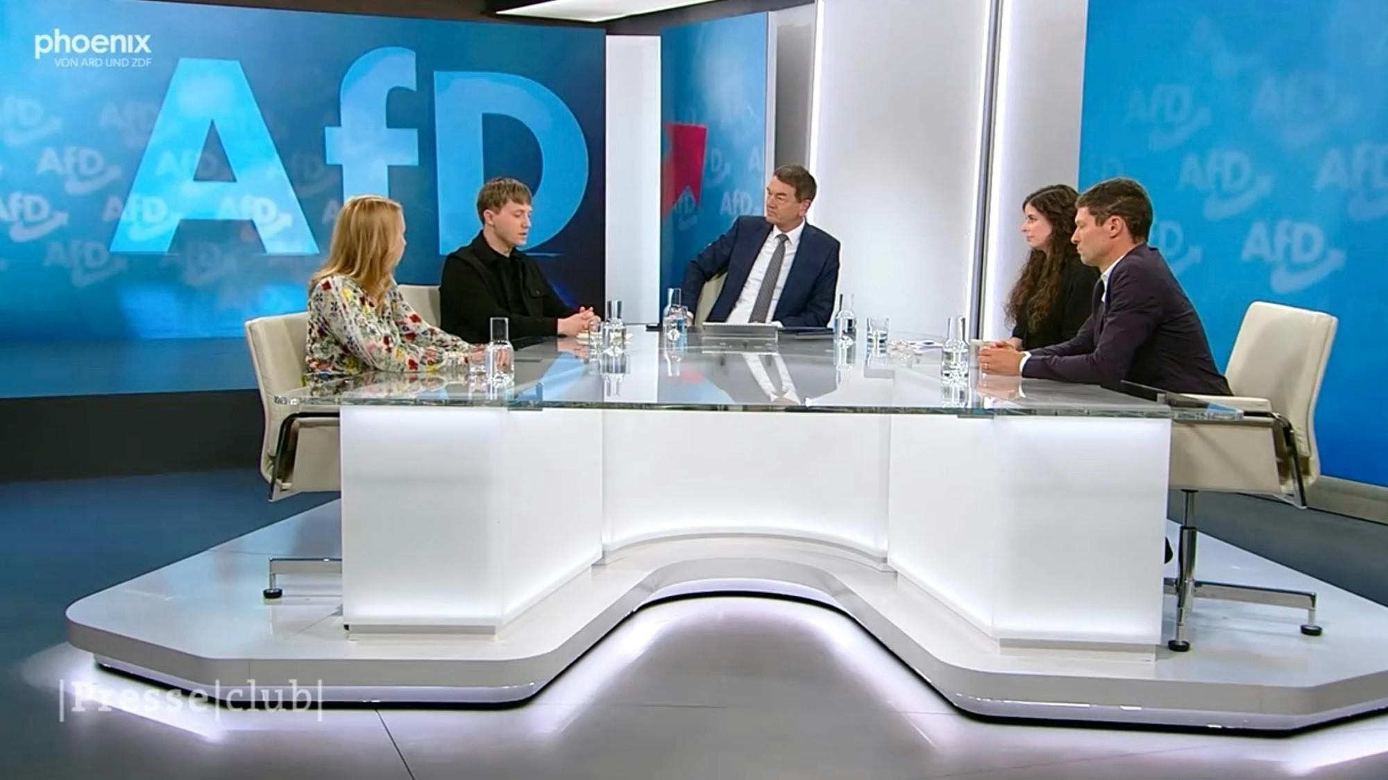 Screenshot des Presseclubs. Das gesamte Studio ist gesäumt von AfD-Logos in unterschiedlichen Größen, es mutet an wie ein Parteitag