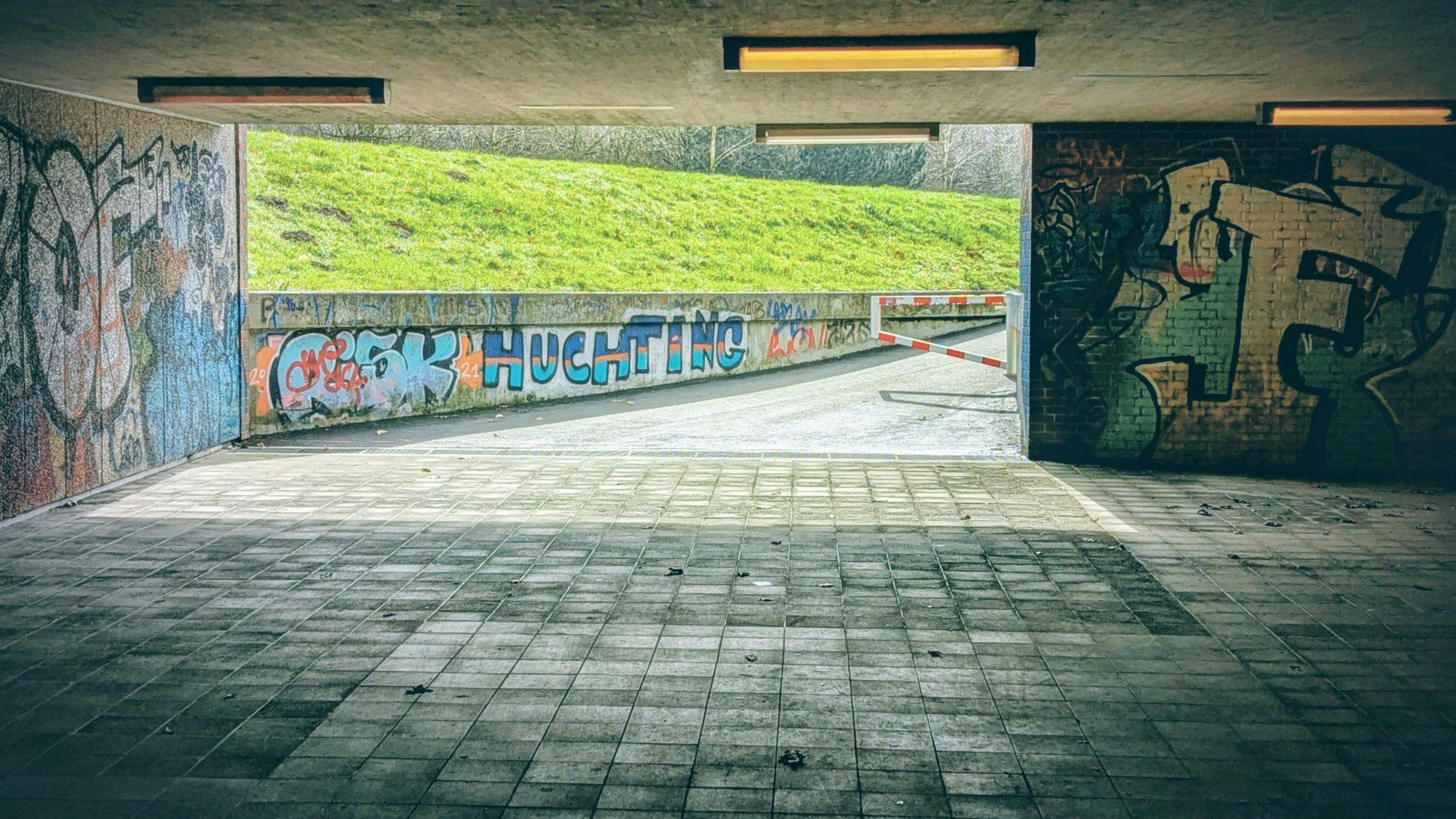 Ein Fußgängertunnel, der nach draußen ins Helle führt. Auf einer Betonwand steht ein Graffito: Huchting.