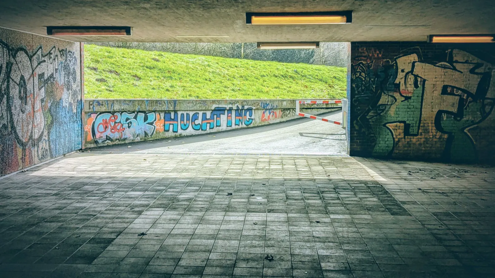 Ein Fußgängertunnel, der nach draußen ins Helle führt. Auf einer Betonwand steht ein Graffito: Huchting.
