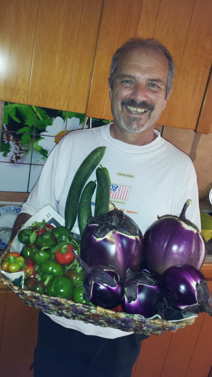 Un uomo felice mostra quello che ha raccolto nel suo orto: melanzane, cetrioli e peperoncini.