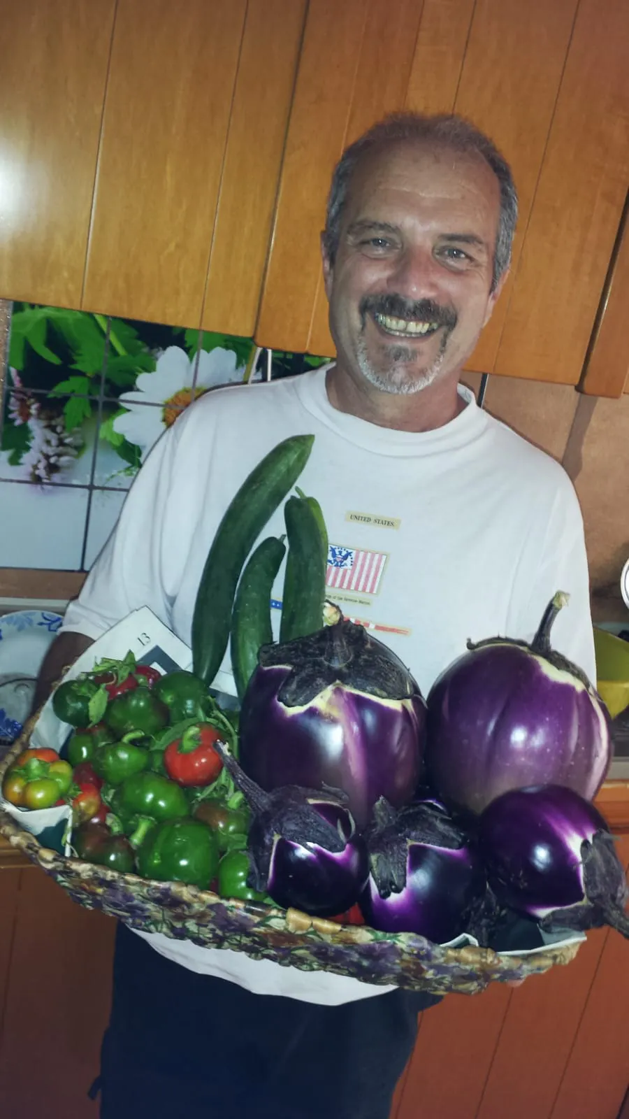 Un uomo felice mostra quello che ha raccolto nel suo orto: melanzane, cetrioli e peperoncini.