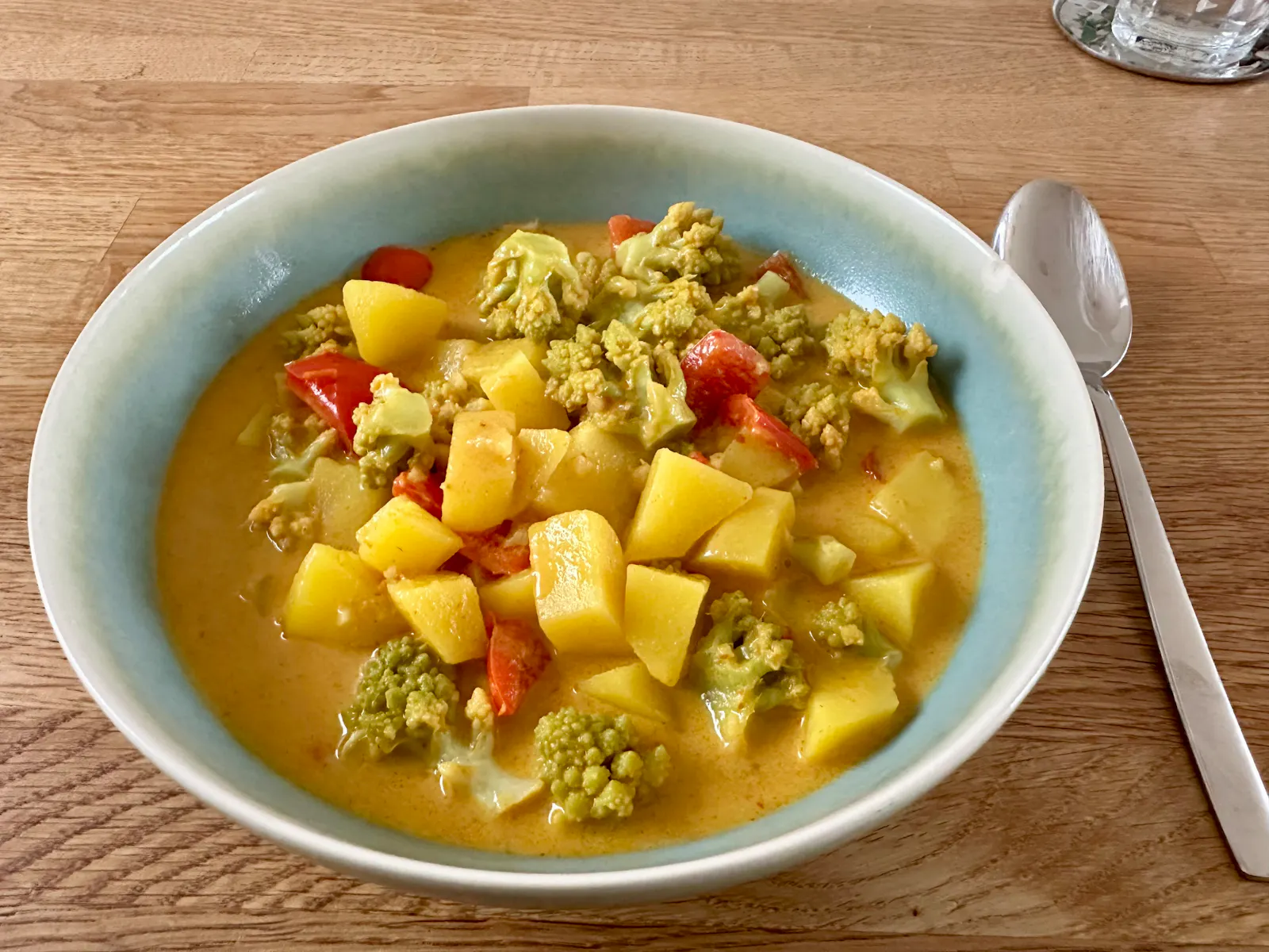 Tiefer, grüner Teller mit gelbem Curry mit Romanesco-Blumenkohl, Kartoffeln und Roter Paprika.