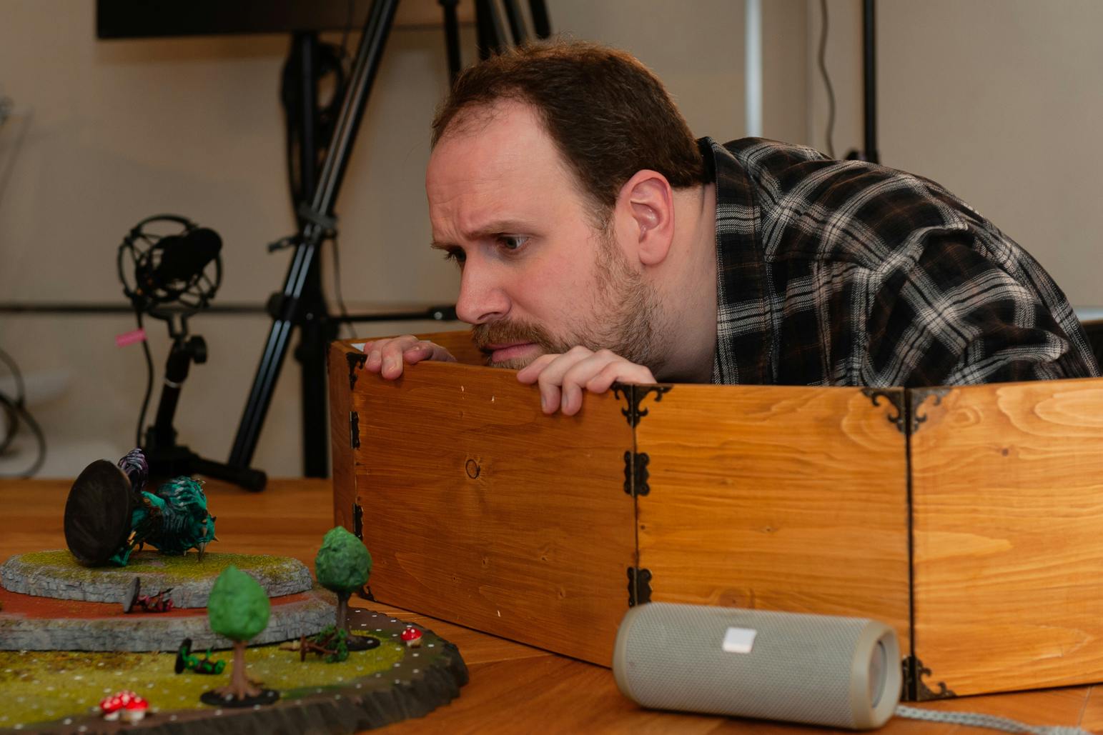 Alex blickt besorgt über seinen Spielleiterschirm und hält ihn mit beiden Händen fest. Einige Miniaturen liegen besiegt auf dem Schlachtfeld. Es ist keine Szene aus einer tatsächlichen Episode, sondern gestellt.
