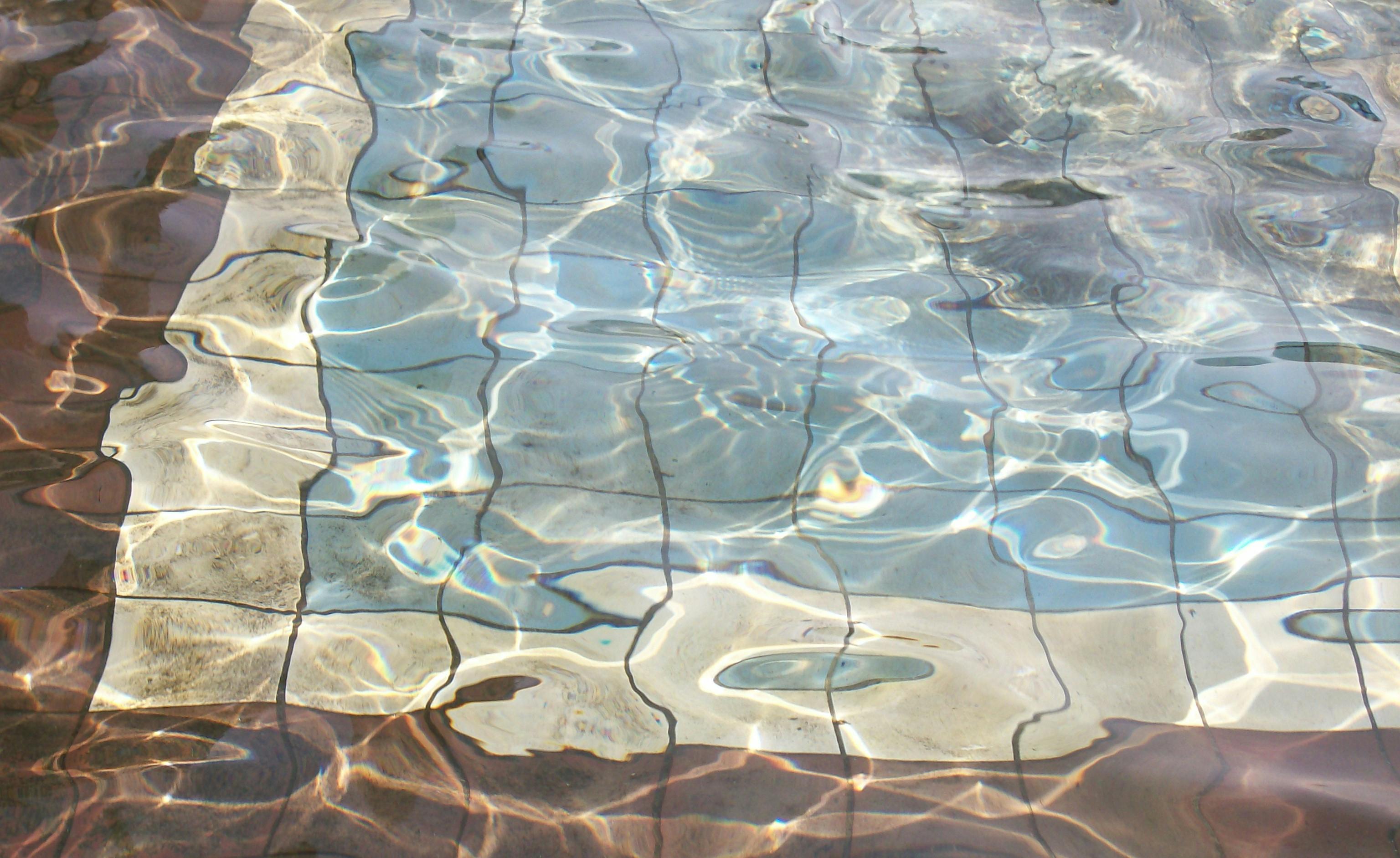 Wasser in einem Becken, der Boden des Beckens ist braun, beige und blau. Das Wasse rschlägt leichte Wellen und schimmert in der Sonne.
