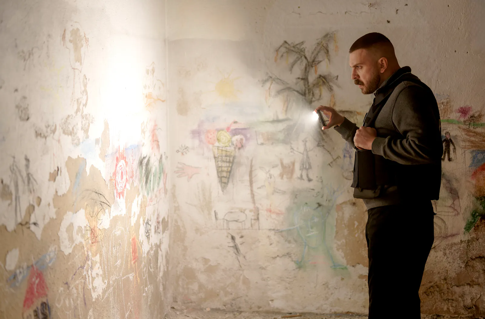Hamza Kulina (Edin Hasanovic) in einem Nebenraum der Lichtsekte, mit Taschenlampe schaut er sich Wandkritzeleien an © HR/Sommerhaus/Tatiana Vdovenko