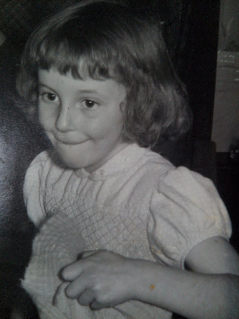 A girl facing left with a very mischevious expression. She is wearing a puff sleaved smocked dress.