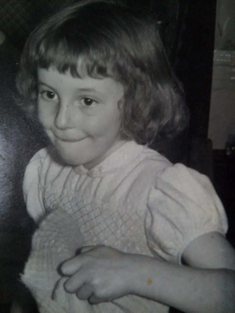 A girl facing left with a very mischevious expression. She is wearing a puff sleaved smocked dress.