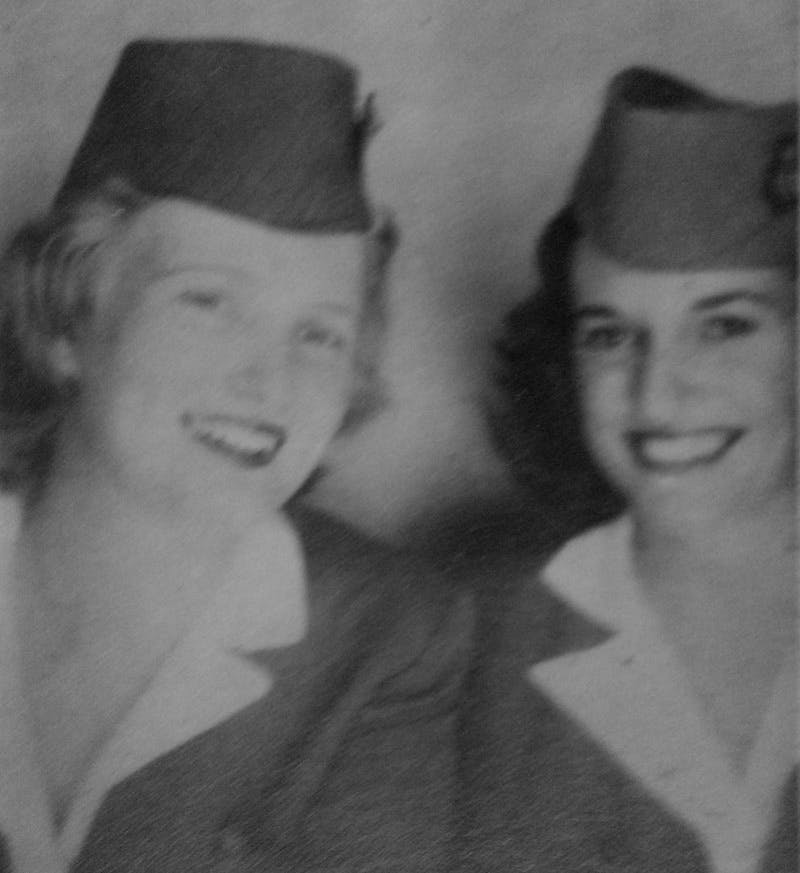On the left is a blond woman, Ruth de Roux, and on the right is her friend who as dark hair. They are both smiling, are wearing hats and dressed in the uniform of an airline: The British West Indian Airways