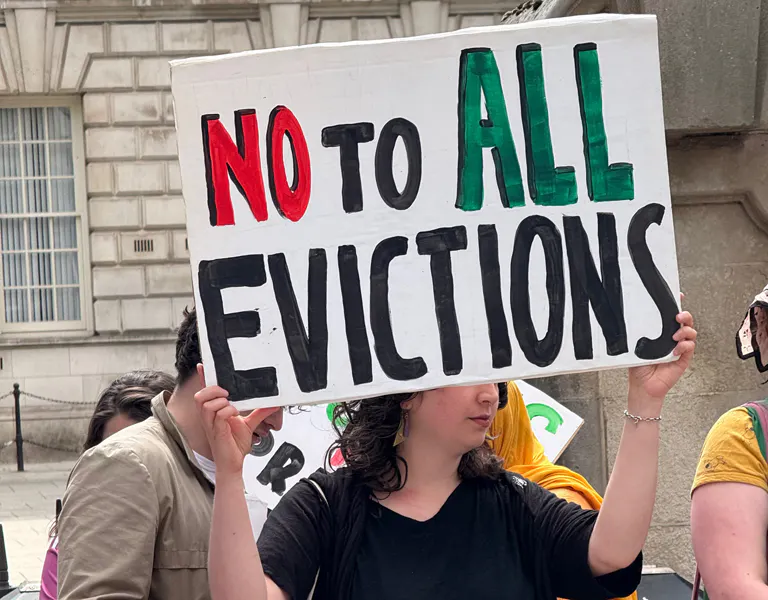 Image shows a woman holding up a placard which reads 'No to all evictions'