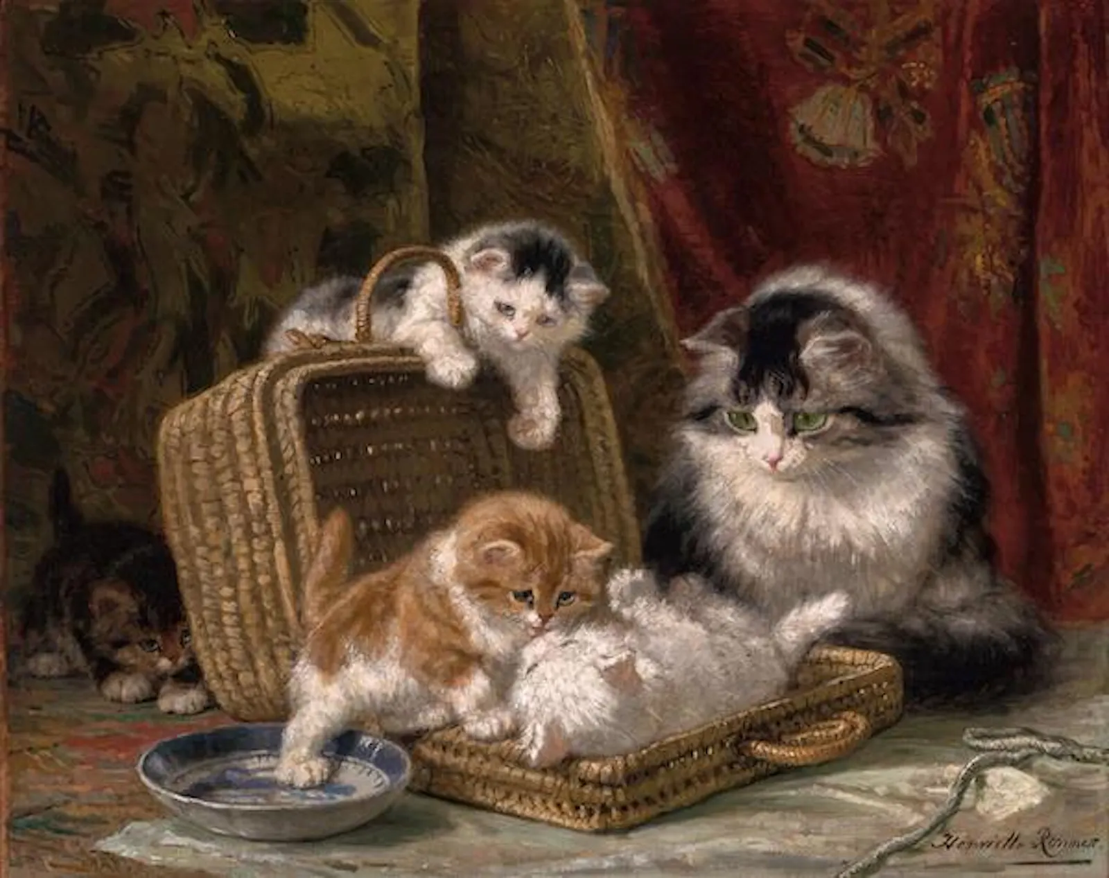 Tres gatitos juegan con un cesto bajo la atenta mirada de su madre. Una escena dulce.