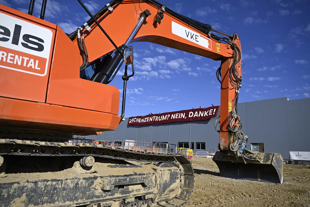 Foto von der Baustelle. Es zeigt einen Bagger und dahinter das Gebäude mit dem Transparent "Rechtenzentrum? Nein, Danke!"