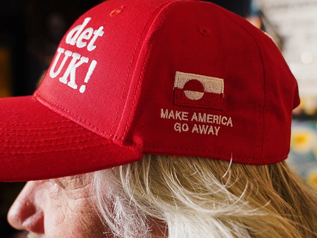 Eine rote cap mit weißer Schrift, auf der vorne “Nu det NUUK!” Und an der Seite unter einer Grönland-Flagge “Make america go away” steht