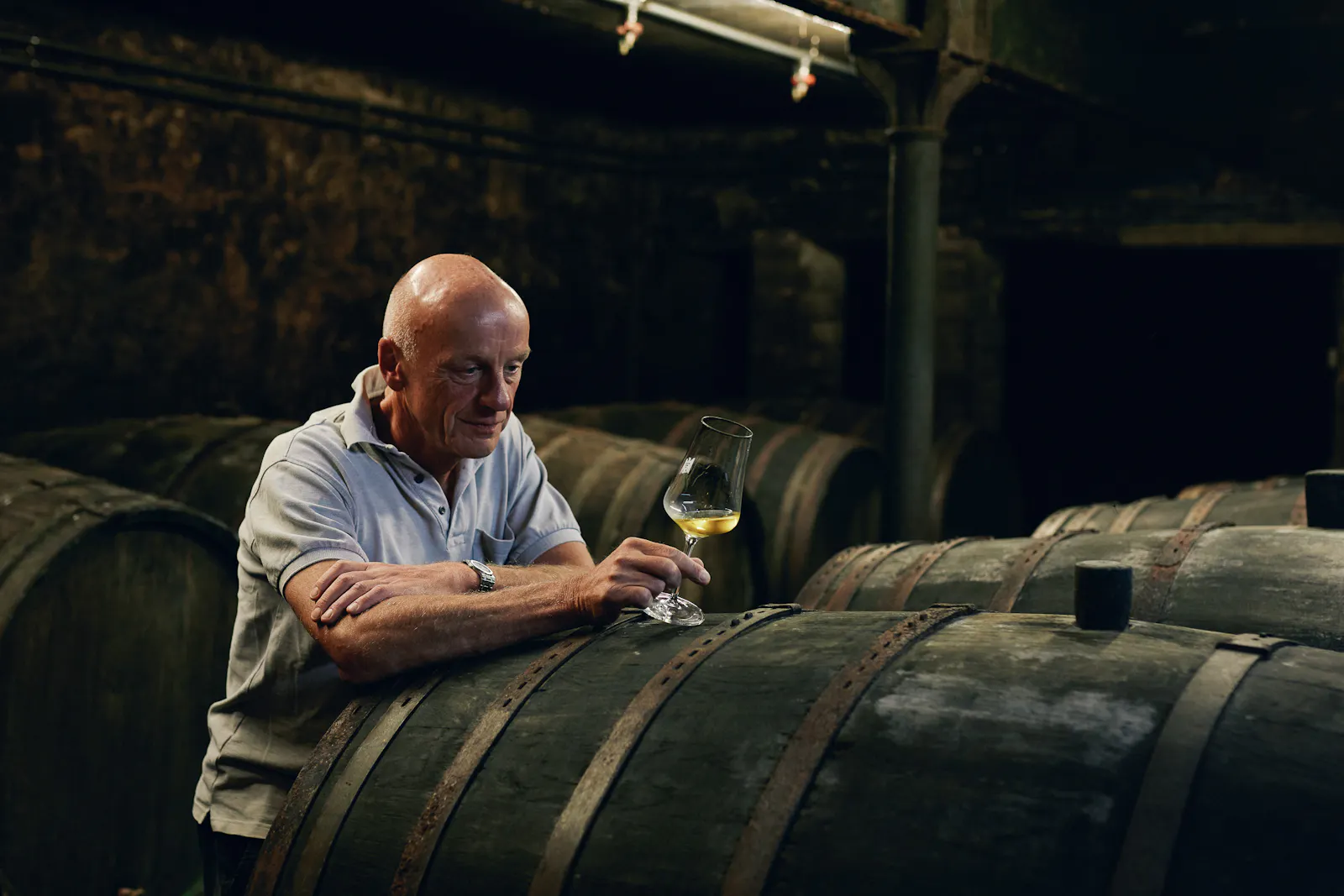 Der Winzer Egon Müller steht in seinem Weinkeller und hat ein Glas mit Weißwein in der Hand.