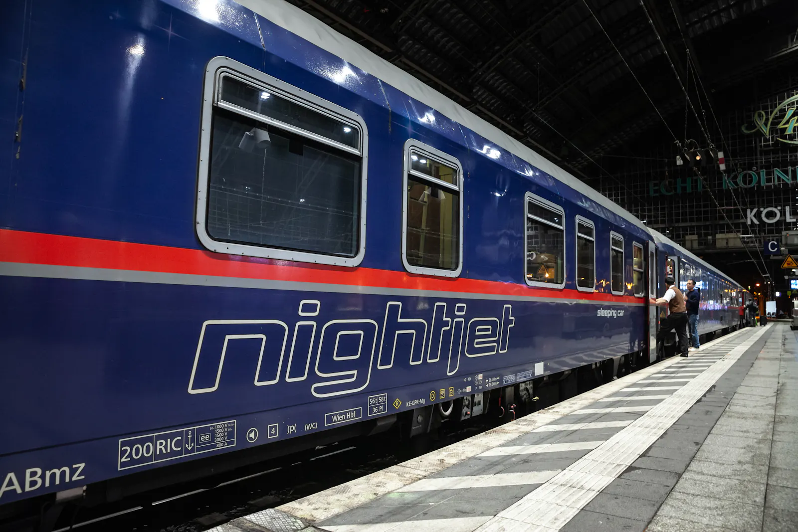Das Foto zeigt einen blauen Nightjet-Nachtzug der ÖBB. Er steht im Bahnhof. Menschen steigen ein.
