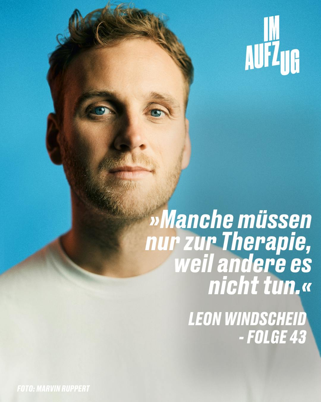 Auf dem Bild ist ein Mann mittleren Alters zu sehen, der direkt in die Kamera blickt und ein leichtes Lächeln zeigt. Er hat kurzes, welliges Haar und trägt ein schlichtes weißes T-Shirt. Der Hintergrund des Bildes ist ein einheitliches, beruhigendes Blau, das gut zum hellen Thema des Porträts passt. Im oberen linken Bereich ist der Text "IM AUFZUG" in weißen Buchstaben zu lesen. Im unteren Teil des Bildes steht ein Zitat: "Manche müssen nur zur Therapie, weil andere es nicht tun." Dieses wird "LEON WINDSCHEID - FOLGE 43" zugeschrieben, was darauf hindeutet, dass es sich um ein Zitat von ihm aus der Episode 43 einer Serie oder eines Podcasts handelt. Unterhalb des Zitats befindet sich der Vermerk "FOTO: MARVIN RUPPERT", was den Fotografen des Porträts angibt.