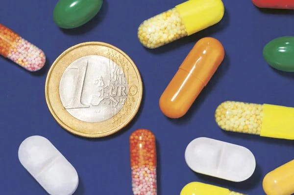 Viele bunte Pillen neben einem Euro auf blauem Hintergrund.