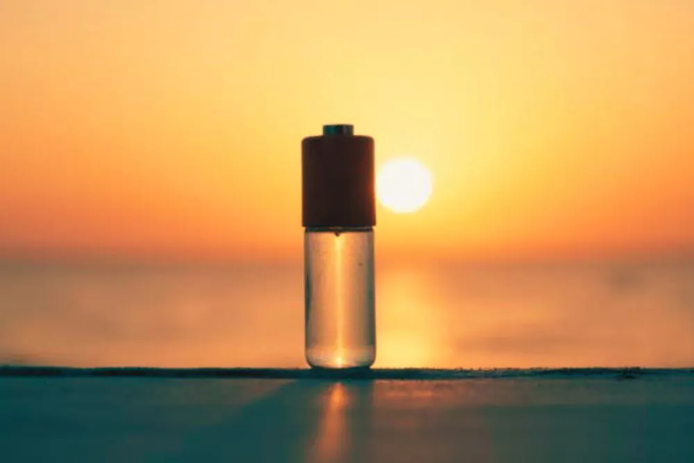 Une pile AA transparente en verre, remplie de liquide, est posée dehors, face au soleil levant.