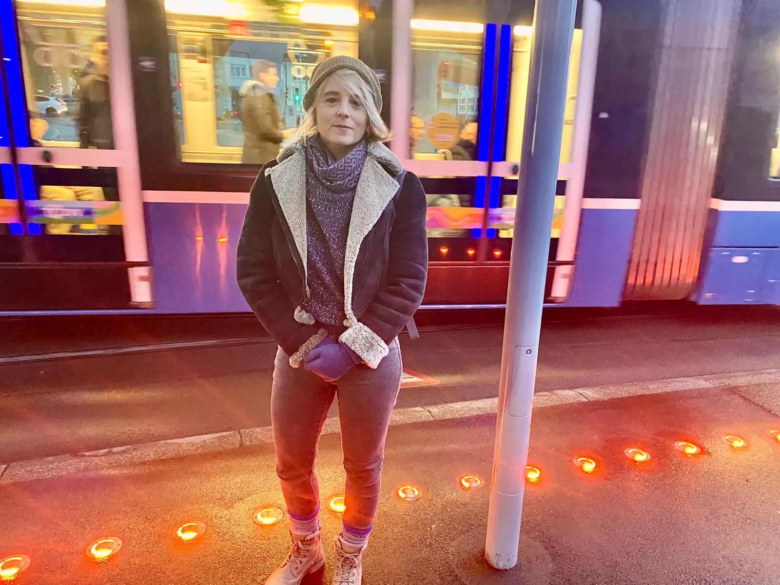 Das Bild zeigt die Politikerin Sandra Bienek auf dem Escher-Wyss-Platz in Zürich. Im Hintergrund ein durchfahrendes Tram, vorne am Boden rote Warnlichter.
