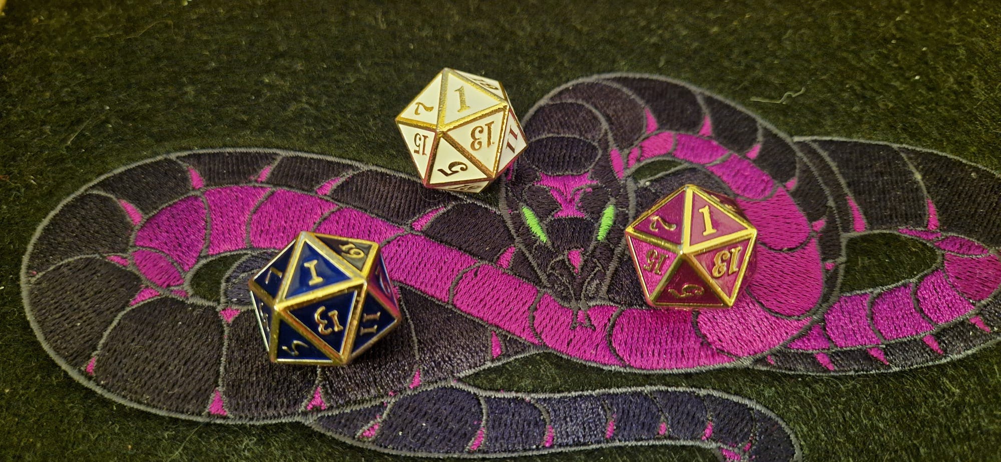 Drei zwanzigseitige Würfel, die jeweils eine 1 zeigen, in einem Dice Tray der Verhüllten Schlange.
