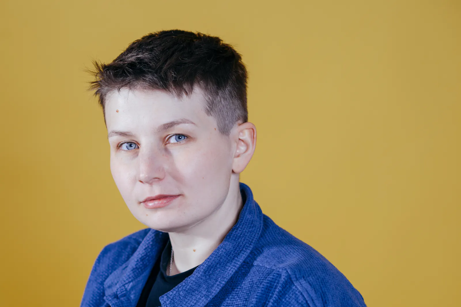Sara Grzybek lächelt, im blauen Jeanshemd vor gelbem Hintergrund