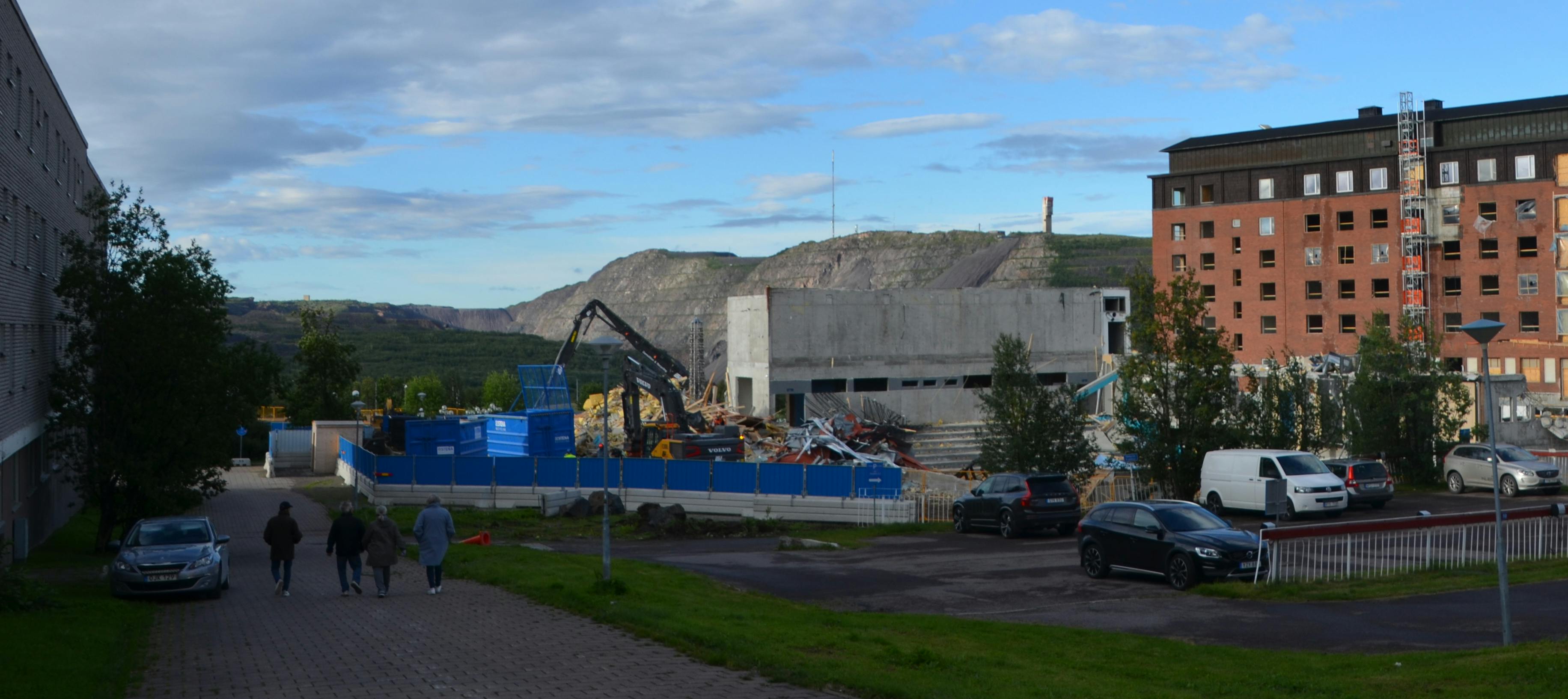Bagger, Zaun,  Gebäudereste, im Hintergrund Berg