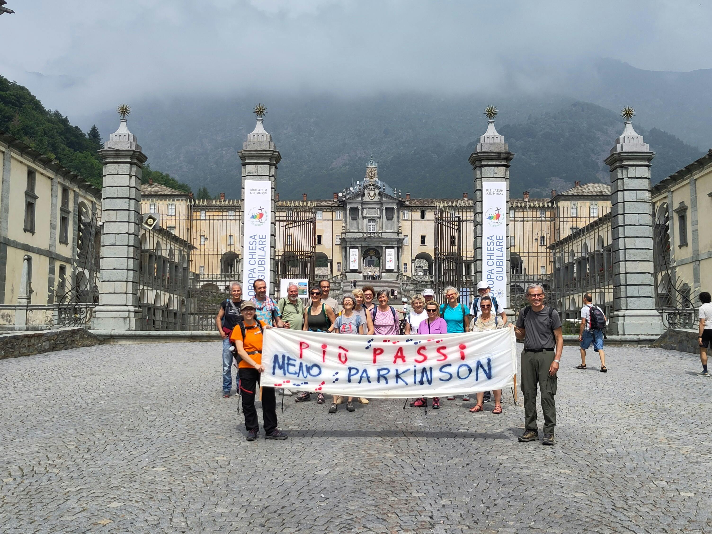 Arrivo di Senza tremori ad Oropa. Striscione retto da giovane a sinistra e non più giovane a destra. Dietro lo striscione il  gruppo e sullo sfondo il Santuario di Oropa