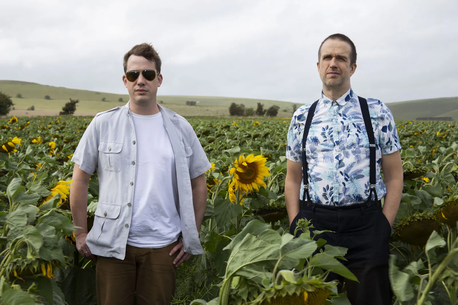 The Quietus cofounders Luke Turner and John Doran stand in a field of sunflowers, looking ambivalent.