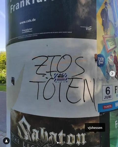 Auf einer Litfaßsäule ist mit schwarzem Filzstift groß die antisemitische Parole „ZIOS TÖTEN“ geschrieben. Das Wort „Zios“ ist eine abwertende Abkürzung für Zionist:innen und wird in antisemitischen Kontexten häufig synonym für Jüdinnen und Juden verwendet. Die Schmiererei ist teilweise über ein Plakat gekritzelt, das für eine Veranstaltung in Frankfurt wirbt. Rechts im Bild sind weitere Plakate zu sehen.